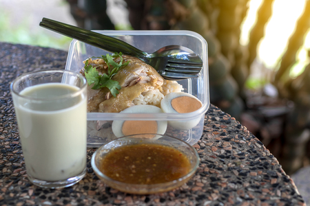 Chicken rice and boiled eggs are packed in a plastic box with soy milk placed on a stone table with bamboo as a backdrop.の写真素材