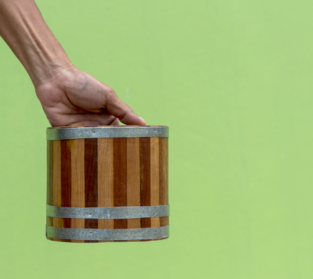 Close-up image of a small wooden bucket Ancient pattern, which was carried by a male hand with a green wall as a background.の写真素材