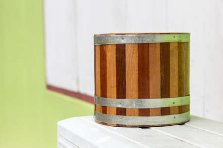 Close-up image of a classic old wooden bucket on a white steel pedestal with a window in the background.の写真素材