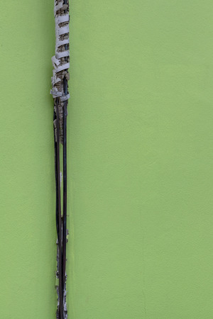 Close-up of old black power cable, worn down, adjacent to the concrete wall, green as a backdrop.の写真素材