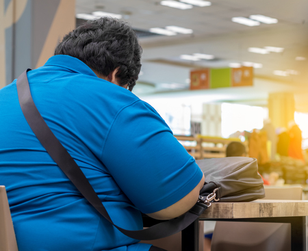 Close-up image of a fat man wearing a blue shirt with a black bag placed on a wooden table inside a department store.の写真素材