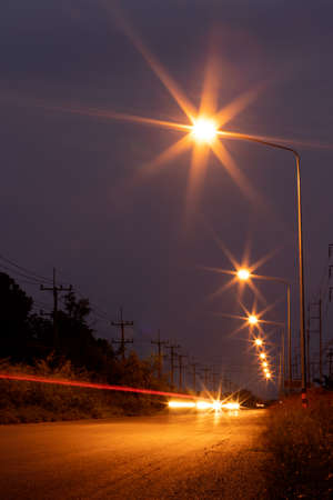 Low-angle view, sparkling orange light from a row of lanterns and car headlights sailing past on a...