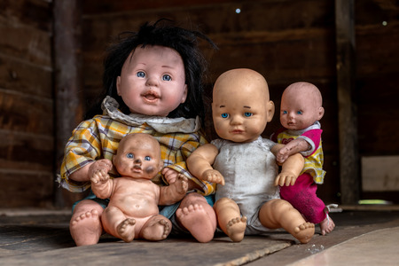 Close-up of a family of plump baby dolls smiling happily sitting on a wooden floor in an old house.の写真素材