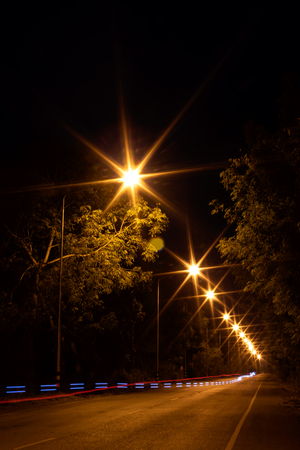 Scenic views of light from lanterns and car headlights, which sail on a dirt road full of trees in the twilight.の写真素材
