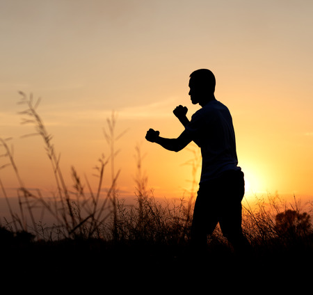 Silhouette sunset light on the side of a man punching fist preparing to fight near the countryside.の写真素材