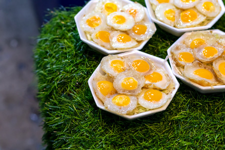 Close-up image of fried crispy quail eggs in a foam box placed on a green artificial grass in a...
