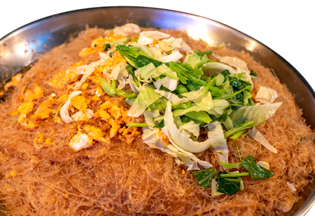 Stir-fried noodles with many vermicelli in a round stainless steel tray, placed on a green canvas in a market.の写真素材