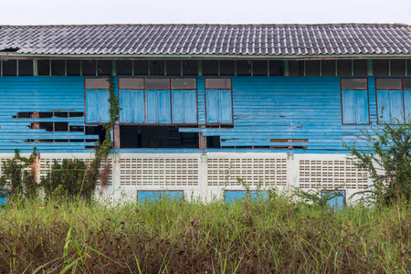 Low view through the grass to the ruins of an abandoned old blue school, which is weathered in the Thai countryside.の写真素材