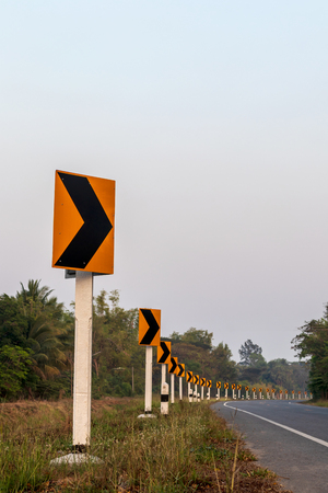 Low view of the row of signs, yellow curves on Thai roads in the daytime, near the forest.の写真素材