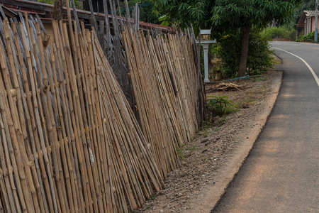 The view of the bamboo fence, which was damaged by a house near the paved road in the Thai countryside.の写真素材