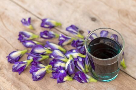Close-up: A cup of green water with purple pea flowers is beautifully placed on the old wooden floor, which is a health-related herb.の写真素材