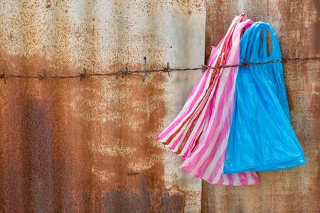 Many colorful plastic bags that were then used to be hung on barbed wire on an old zinc wall of a house.の写真素材