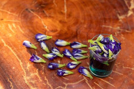 Close-up of a glass of water with beautiful purple butterfly pea flowers laid on a wooden floor, a popular herb.の写真素材