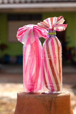 The pink and white striped plastic bags were packed in two clear bottles placed on the pots which were upside down near the walls of a house.の写真素材