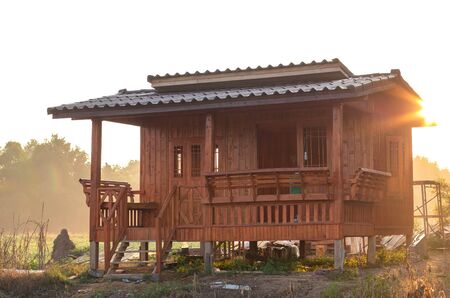 View of a small house made of teak wood, set on the ground with the rising sun in the early morning,...
