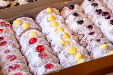 Many donuts are sprinkled with flour and decorated with yellow and red jellies packed in paper boxes for sale.の写真素材