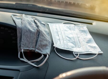 Hygienic masks, both white and gray, are placed on the black console on the inside of the car, where...