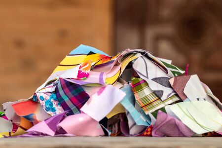 Close-up of many colorful pieces of cloth, stacked on the floor of an old wooden table with a blurred door in the background.の写真素材