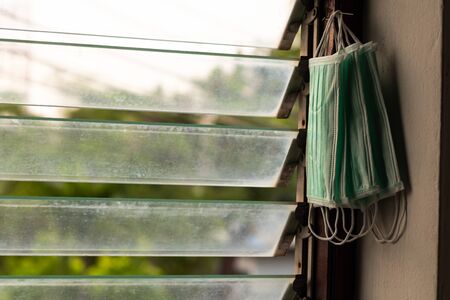 Many green sanitary masks are hung on the wooden frames of louver windows inside a house.の写真素材
