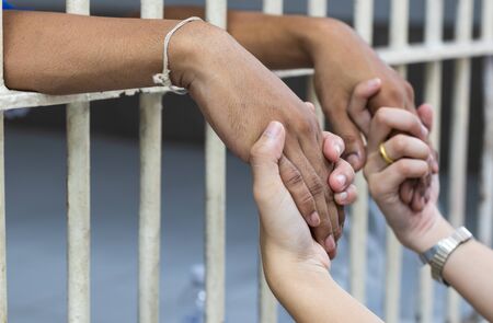 Close-up: The wife is holding the hand of her husband, a prisoner, imprisoned in the white balustrade, showing concern.の写真素材