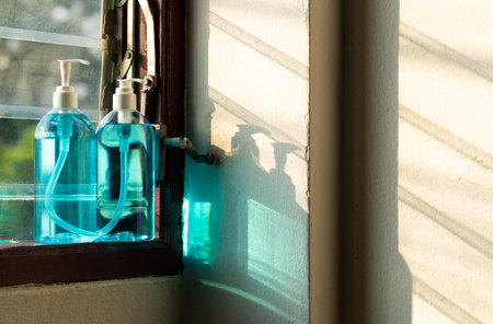Close-up: Both of the blue-colored alcohol spray bottles are standing on a wooden window framing through the sunlight.の写真素材