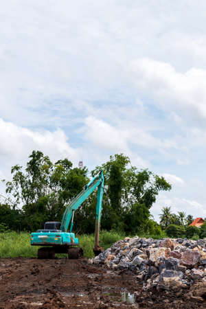A view of the blue backhoe on the muddy ground with granite piles in rural one of Thailand.