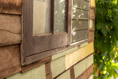 Close-up of the side of the wooden wall and the old window of a house looking out into the light and...