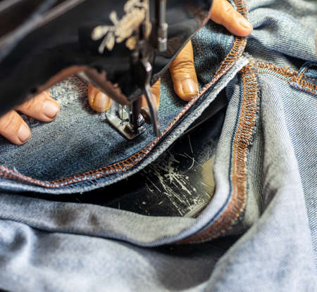 Close-up view, a hand of an elderly Thai woman skillfully repairing a torn jeans fabric with an old...