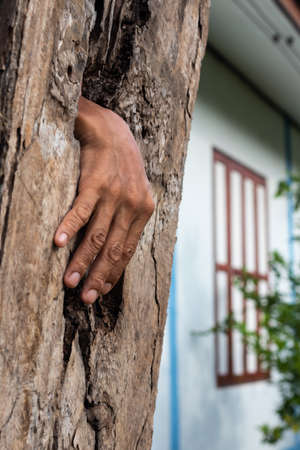 A close-up view, a hand emerged like a ghost from a hole in a weathered decay panel near a house.の写真素材