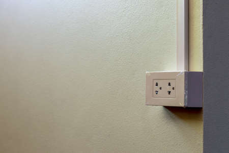 A close-up, a socket-outlet mounted on a white concrete wall inside a new home.