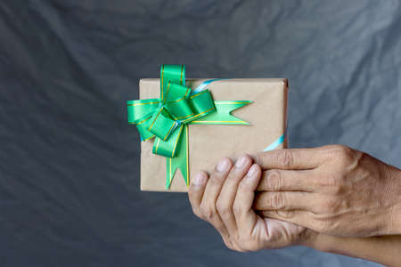 Close-up of a Thai man holding hands holding a gift box made of paper and tied with a beautiful bow with a gray canvas as a backdrop.の写真素材