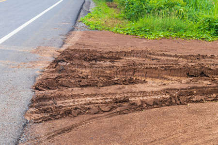 Close to the dirt road surface with wheels traces onto a paved road in rural Thailand.の写真素材