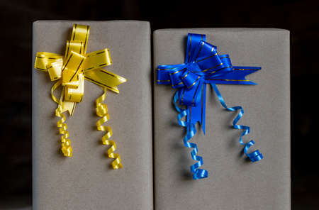Numerous gift wrapping boxes tied in bows with yellow and blue ribbons against a black backdrop.の写真素材