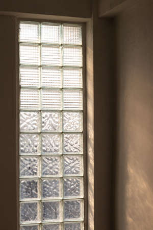 Close-up view of a glass brick wall where the sunlight shines through the day in the corner of a...