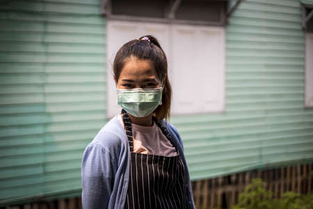 Close-up portrait of a cute and beautiful Thai woman wearing a mask standing near the wall of an old...