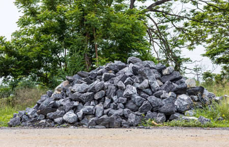 Low perspective Blue granite boulders are piled up on the side of a rural paved road in preparation for dam construction materialの写真素材
