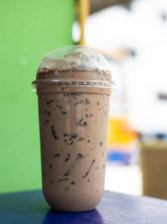 A close-up view of iced coffee drinks in clear plastic cups are placed on a blue tabletop near a...
