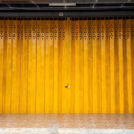 Background The new yellow steel sheet folding door which has been closed and locked is mounted on a...
