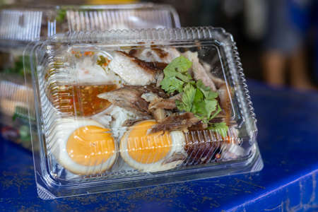 Close-up side view of delicious pork knuckle rice and boiled egg packed in a transparent plastic box placed on a blue background.の写真素材