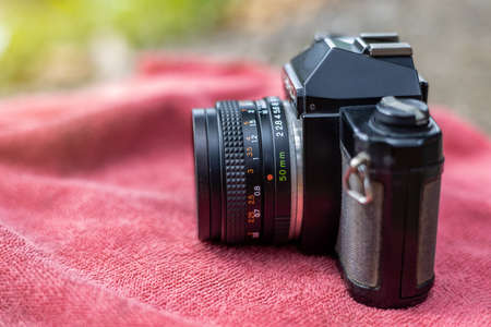 A close-up view of the side of an old black film camera resting on a red towel with blurred green...
