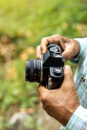 Close-up view from above in the hands of an elderly Thai man carefully holding an old film camera awaiting a photoshoot in a rural Thai area.の写真素材