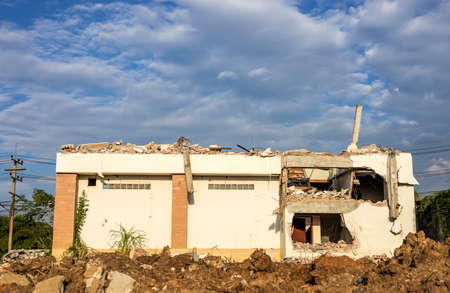 A low angle view of the rubble of an old white abandoned building on the ground that has been demolished for renovations with a cloudy afternoon and a blue sky in the background.の写真素材