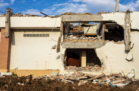 A low angle view of the rubble of an old white abandoned building on the ground that has been demolished for renovations with a cloudy afternoon and a blue sky in the background.の写真素材