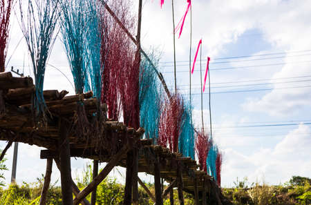 A low, close-up view of a bridge of eucalyptus logs decorated with brightly colored twigs, stretching along a cloudy road as a backdrop in the agricultural countryside of Thailand.の写真素材