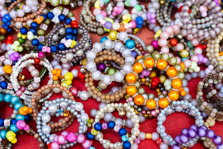 A close-up background of numerous bracelets made of colorful beads stacked on a red cloth for retail...