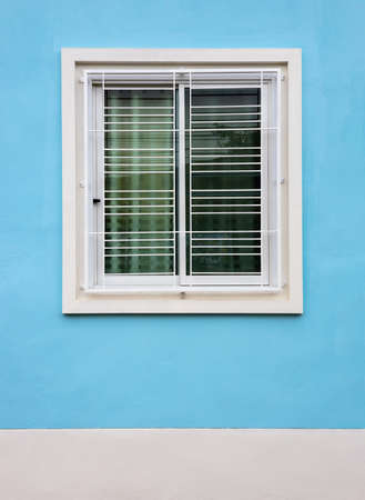 Close-up view, background of white concrete window frames with wrought-iron grilles mounted against blue walls, is part of a common house in rural Thailand.の写真素材