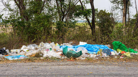 View of piles of plastic waste dumped on the side of a road near the trees and rice fields that are common in rural Thailand.の写真素材