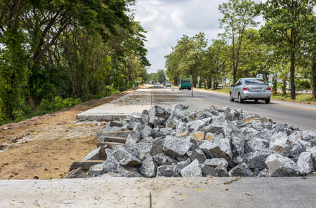 Low angle view of piles of concrete rubble from demolition destroying old road for renovation near roadside trees during daytime in Thai countryside.の写真素材