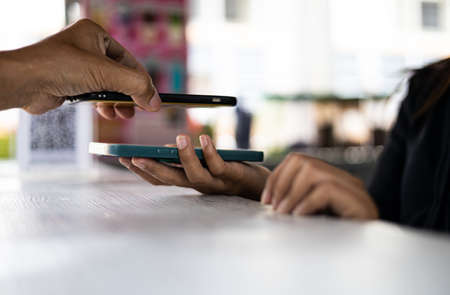 Close-up view of a man's hand scanning a QR code with a mobile phone to pay a coffee shopkeeper who is holding another phone on the counter.の写真素材