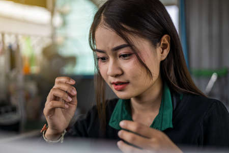 Close-up portrait of a beautiful Thai woman with a puzzled expression with her hands raised in blurry movements inside her coffee shop.の写真素材